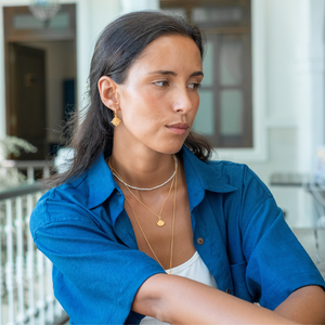 A woman with brown hair in a blue blouse without sleeves and a white top together with golden jewellery