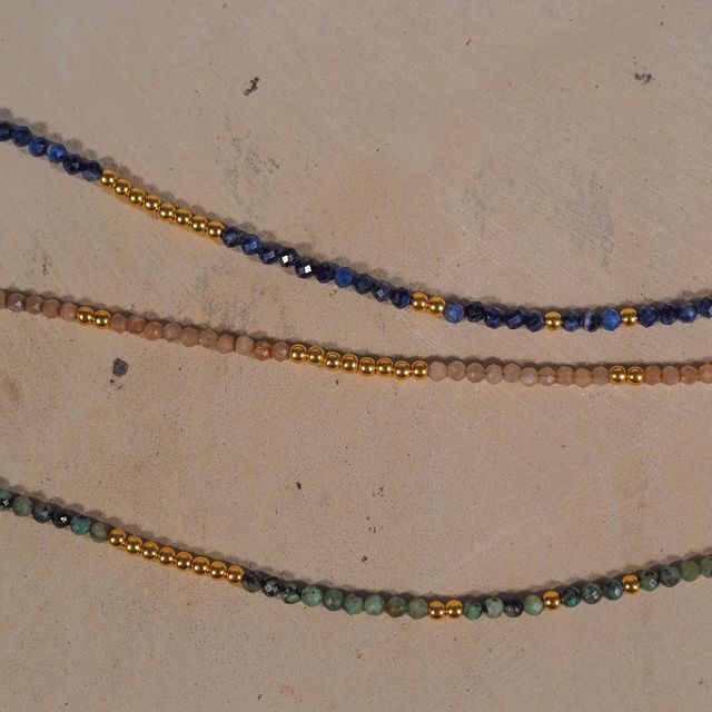 Three delicate gemstone necklaces styled on a blush pink textured backdrop