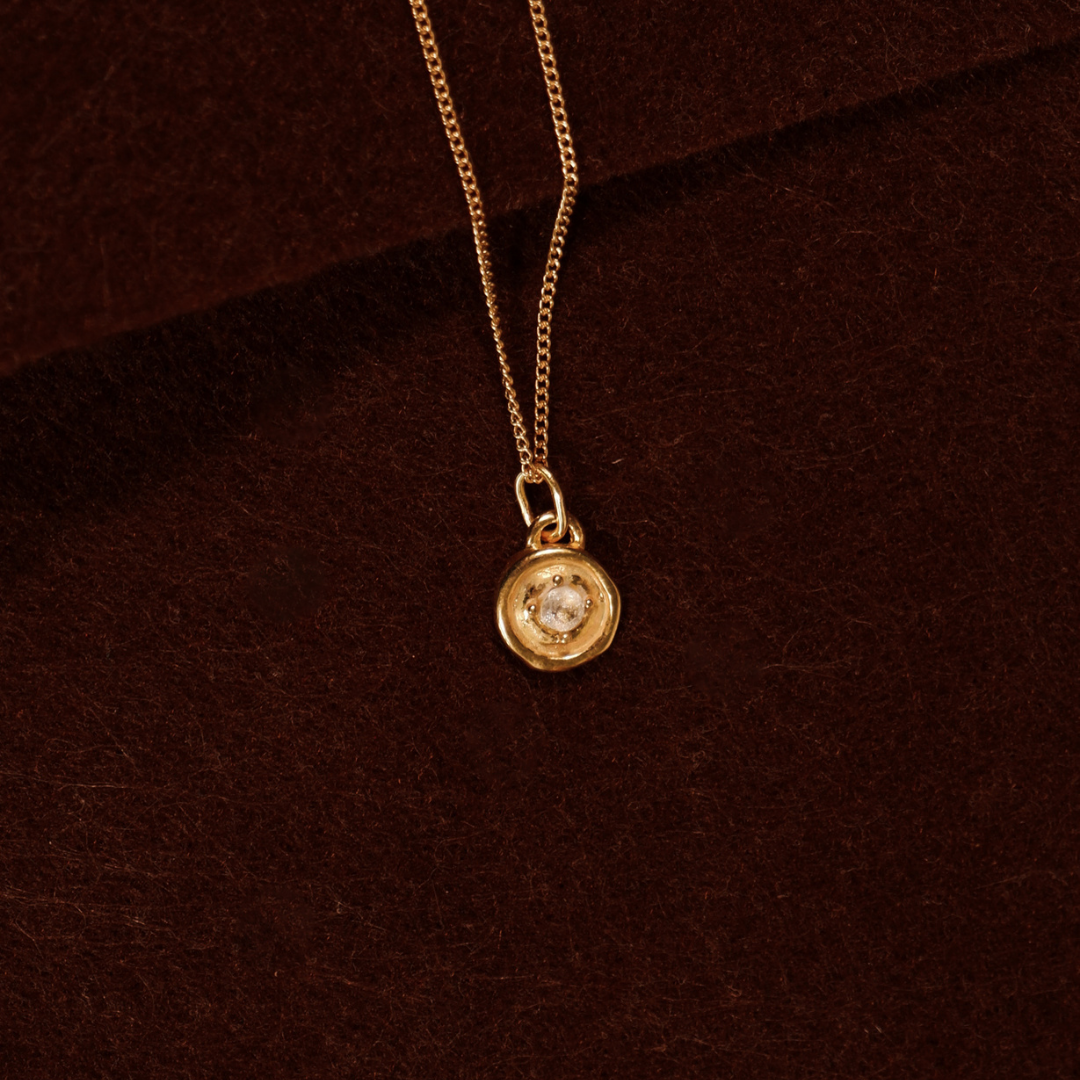 Gold necklace with a round pendant on a brown background