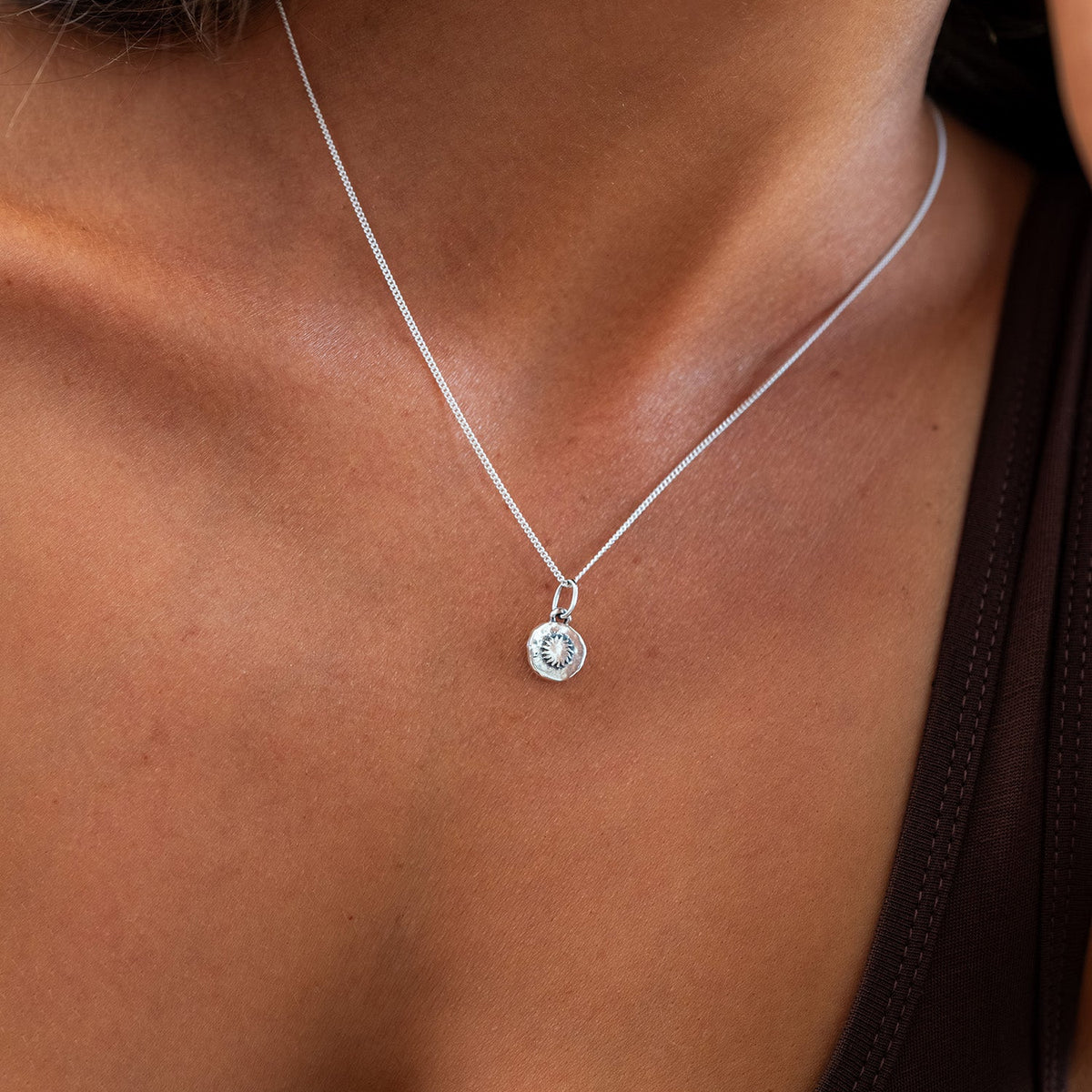 A close-up of a model wearing a delicate silver chain necklace with a small circular silver pendant featuring a clear central stone.