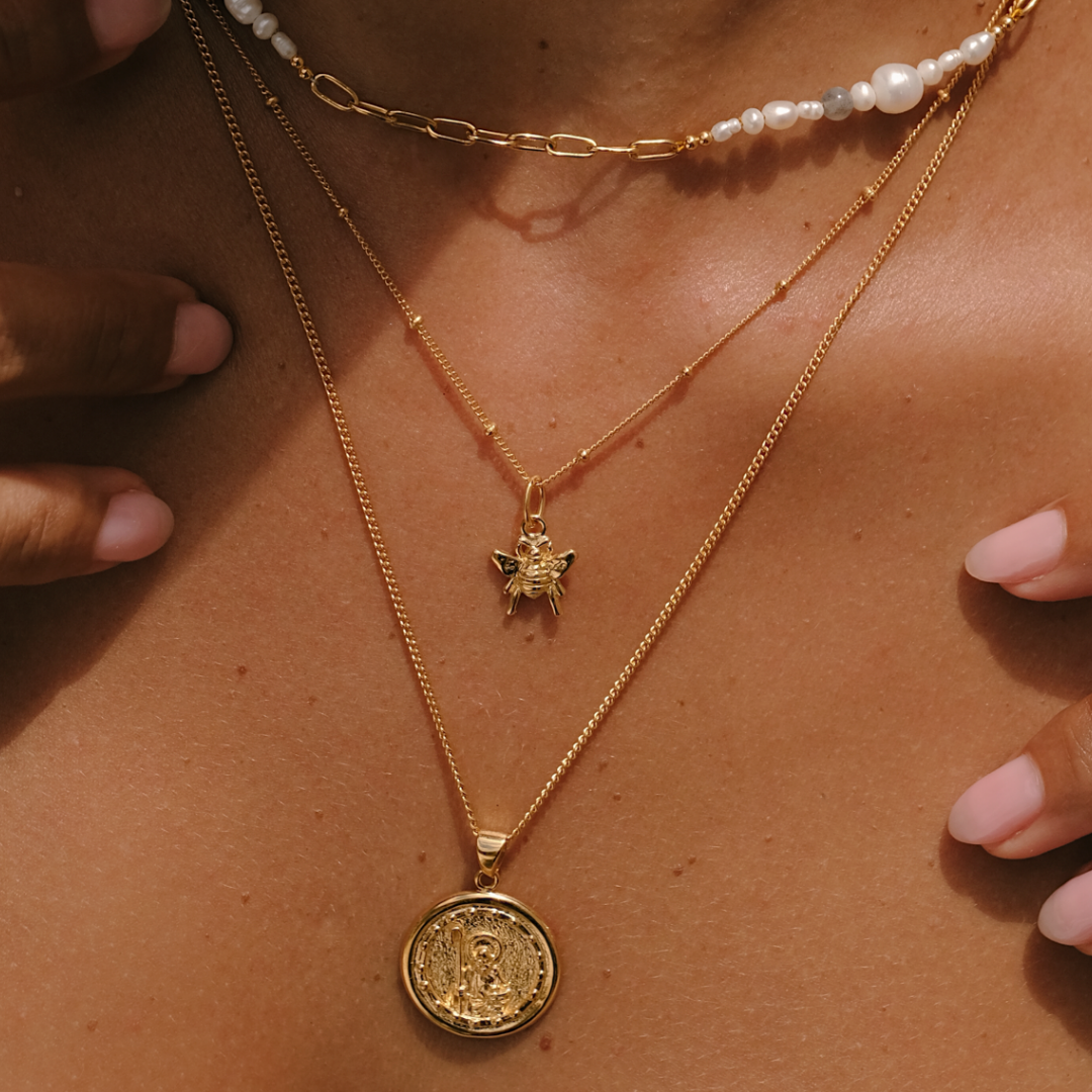 Close-up of a person wearing two gold necklaces with pendants on a brown background