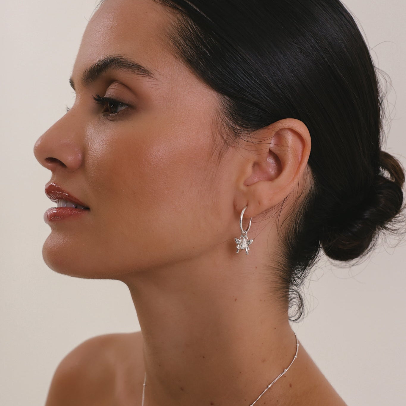 Woman wearing a silver necklace and earrings with a plain background