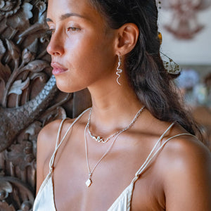 A woman with brown hair wearing two silver necklaces and a snake earring .