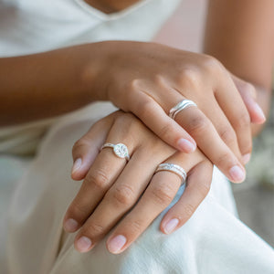 A close-up of two hands wearing multiple silver rings with a white background