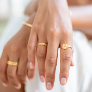 A close-up of two hands wearing multiple golden rings with a white background