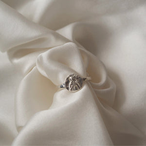 A silver rounded shaped ring elegantly displayed on a gathered white satin fabric.