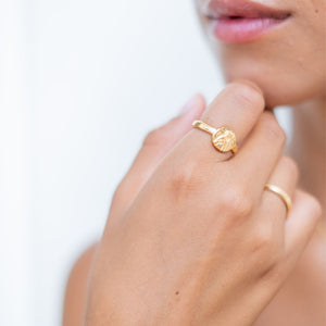 A woman wearing a gold ring featuring an intricately detailed depiction of a saint figure on its face.