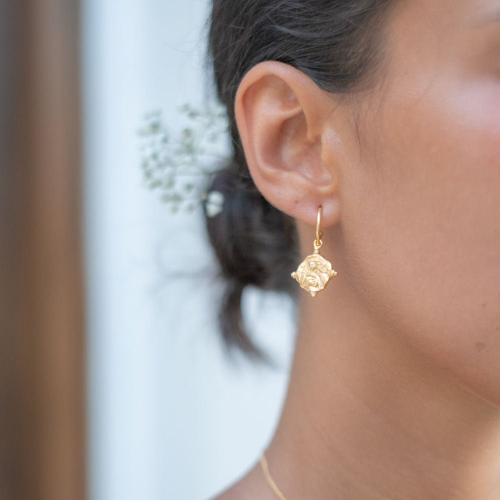 A pair of gold hoop earrings featuring religious figure designs on hanging charms.