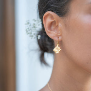 A close-up side view of a woman wearing gold earrings, with her hair styled back to showcase the jewelry.