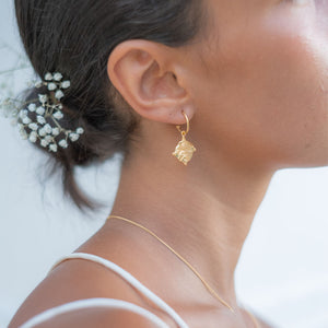 Close up of a woman wearing a gold hoop earring and a delicate gold necklace, with her hair styled in a low bun adorned with small white flowers.