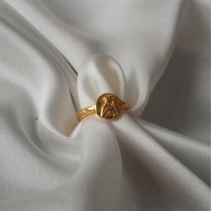 A golden rounded shaped ring elegantly displayed on a gathered white satin fabric.