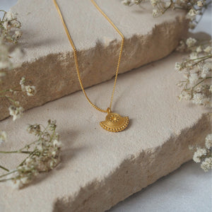 A jewelry display featuring a gold necklace arranged on beige stone pieces with dried flowers.