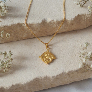 A gold necklace is displayed on a beige stone with delicate white flowers surrounding it.