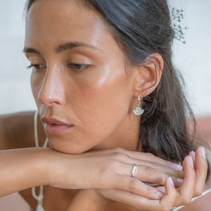 A close-up of a woman with silver sunburst earrings and silver rings, with flowers in her hair.