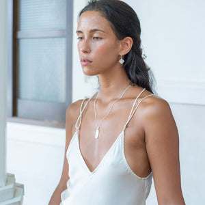 A woman wears a silver hoop earring and a delicate silver necklaces and a white dress.