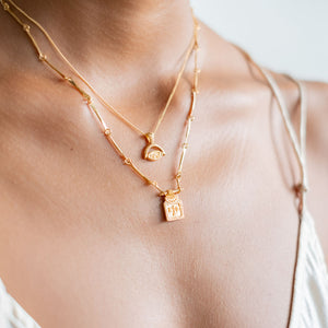 Close-up of a woman wearing two golden necklaces and a white satin dress