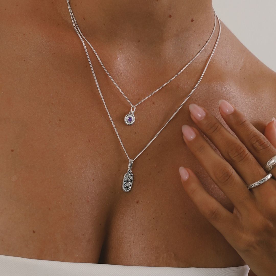 Close-up of a person wearing two silver necklaces with pendants on a neutral background
