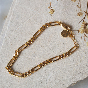 Close-up of a gold chain anklet resting on textured white stones.