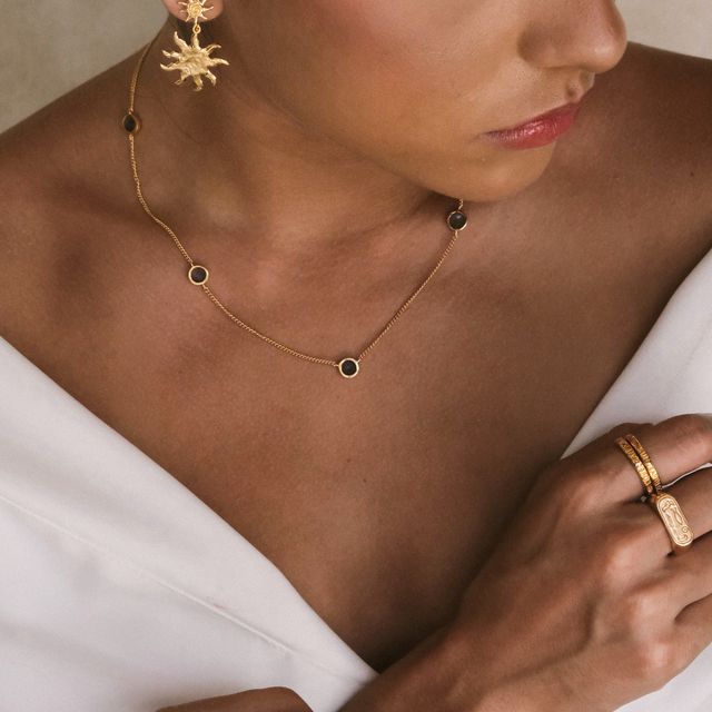 Close-up of a woman styled with a gold gemstone necklace jewelry set including, earrings, and rings