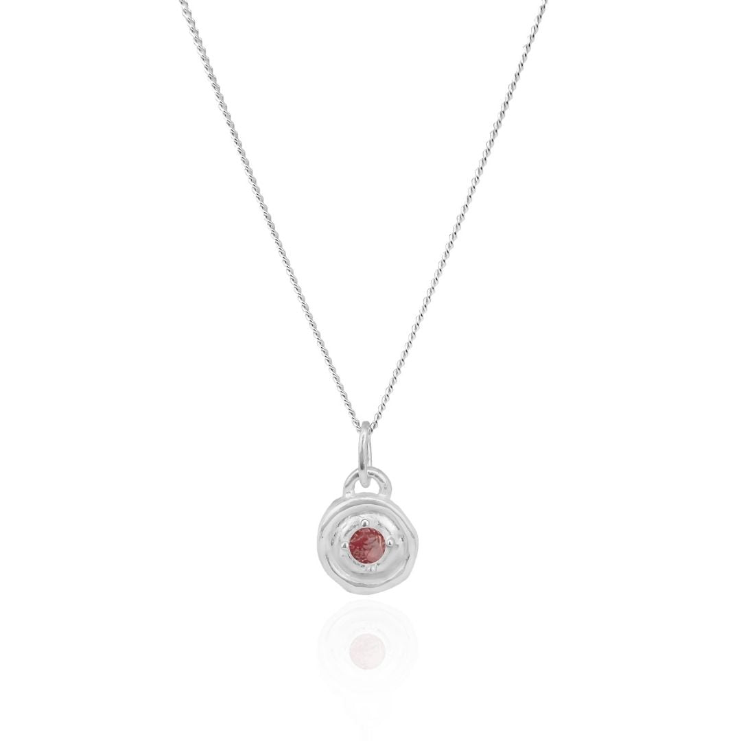 Silver necklace with a circular pendant featuring a red gemstone on a white background