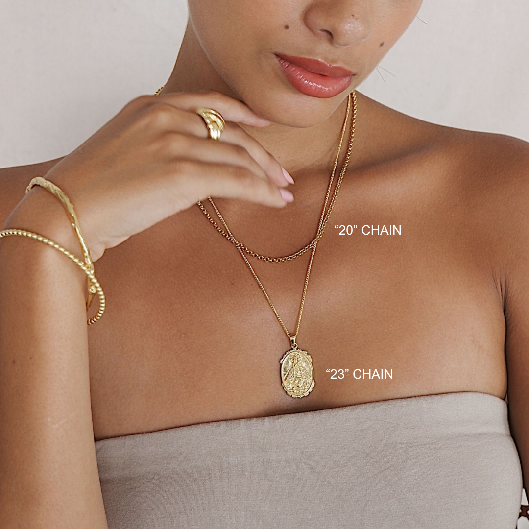 Woman wearing gold jewelry including a necklace and bracelet on a plain background
