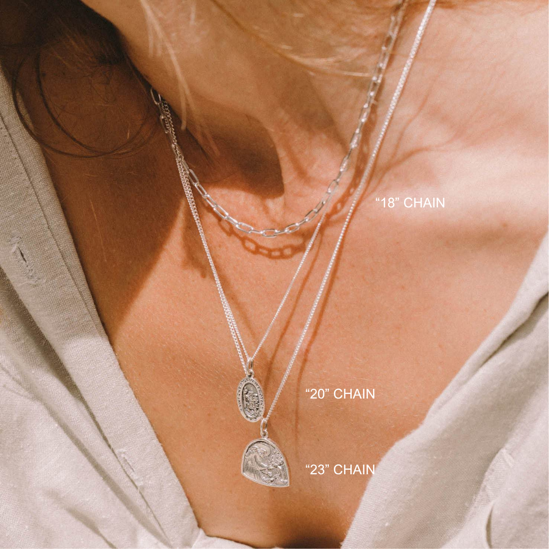 Close-up of layered necklaces with chain lengths labeled on a person wearing a light-colored top.