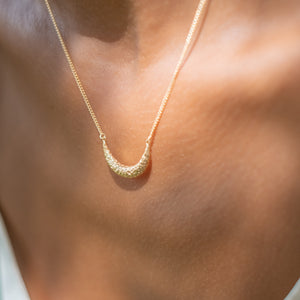 A close-up view of a gold necklace with a crescent moon pendant worn around the neck.