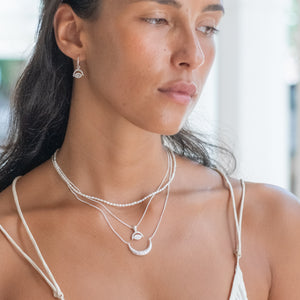 A woman with black hair wearing a silver earring and multiple silver necklaces