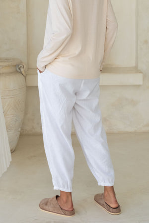 A person with their back turned, wearing white loose-fitting pants and a beige top.