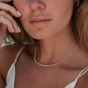 Close-up of a woman's neck and shoulders wearing a thin silver chain necklace and silver hoop earring.