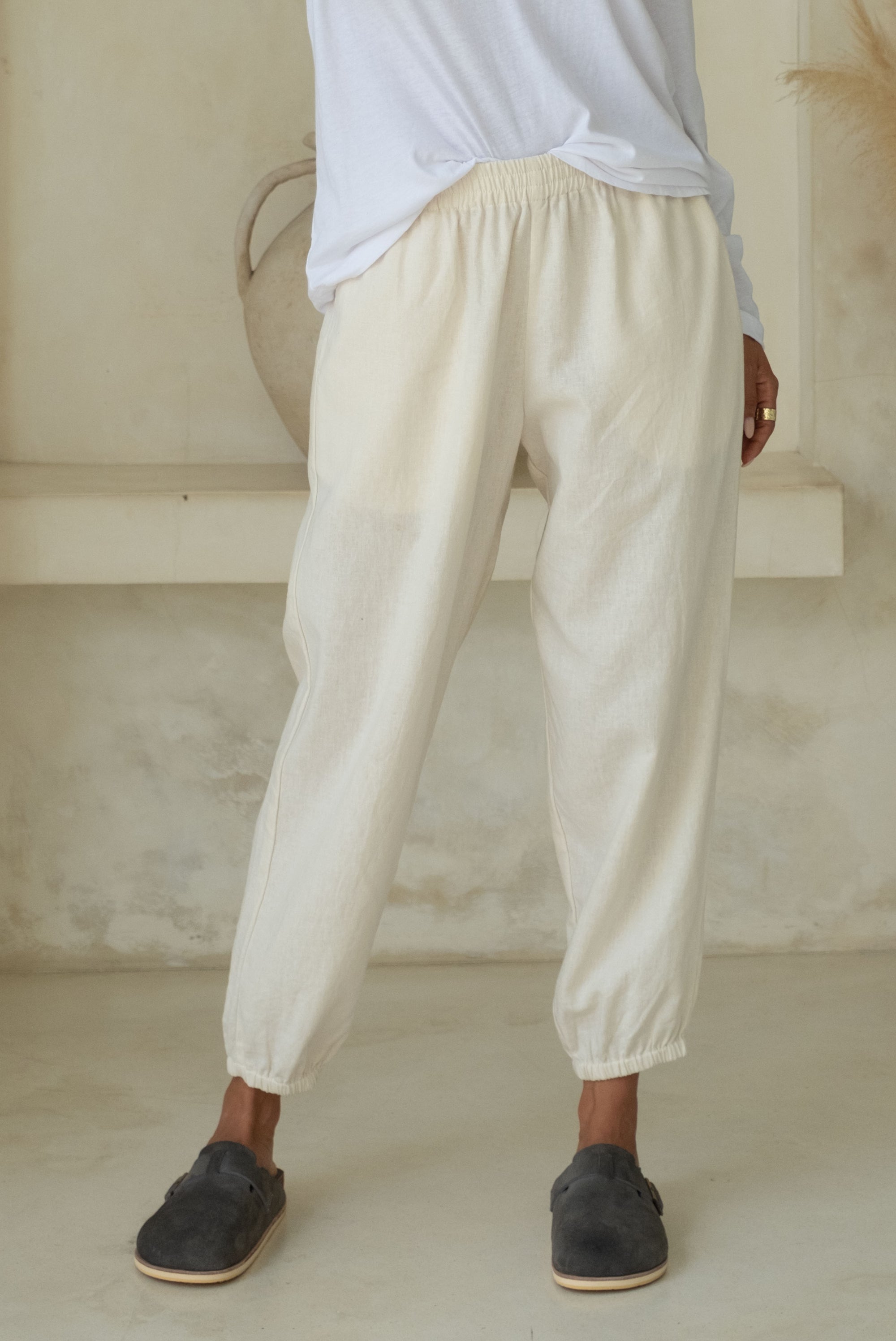 Close-up of light-colored loose pants with an elastic waistband and cuffs, paired with blue slip-on shoes.