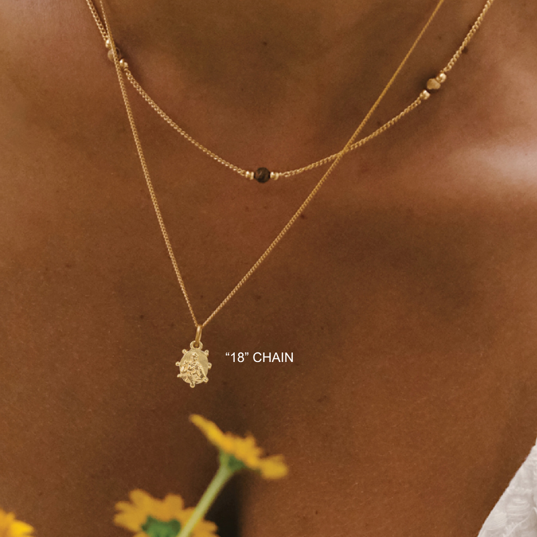 Gold necklace with a star pendant on a person's neck against a brown background with a yellow flower.