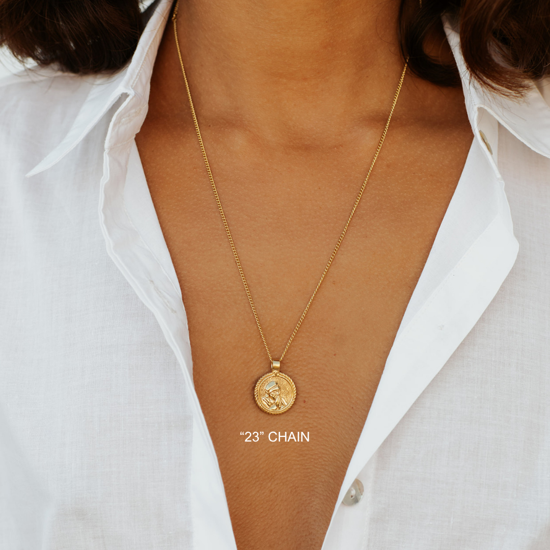 Gold necklace with a pendant on a person wearing a white shirt.