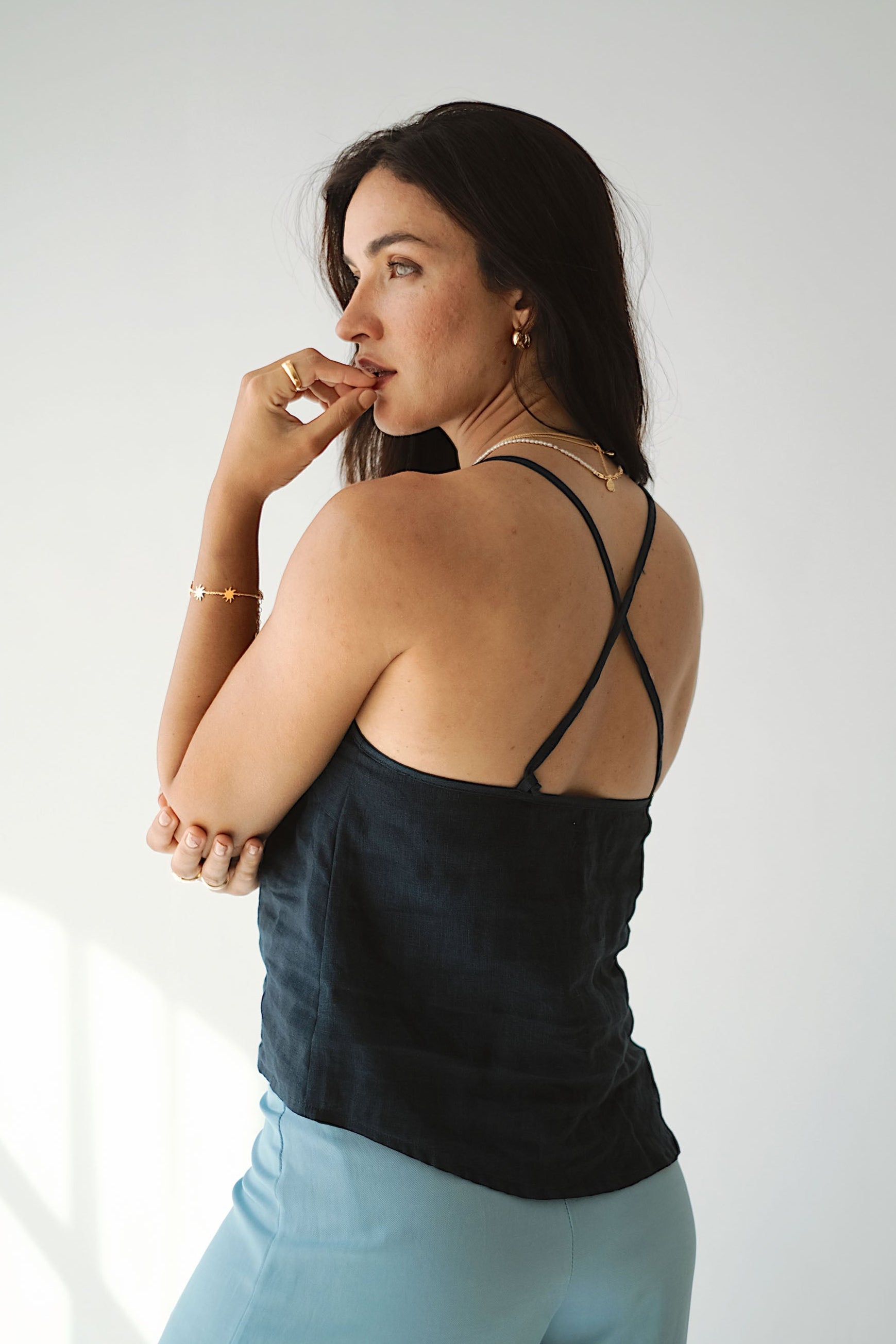 Woman wearing a black strappy top and light blue pants against a white background
