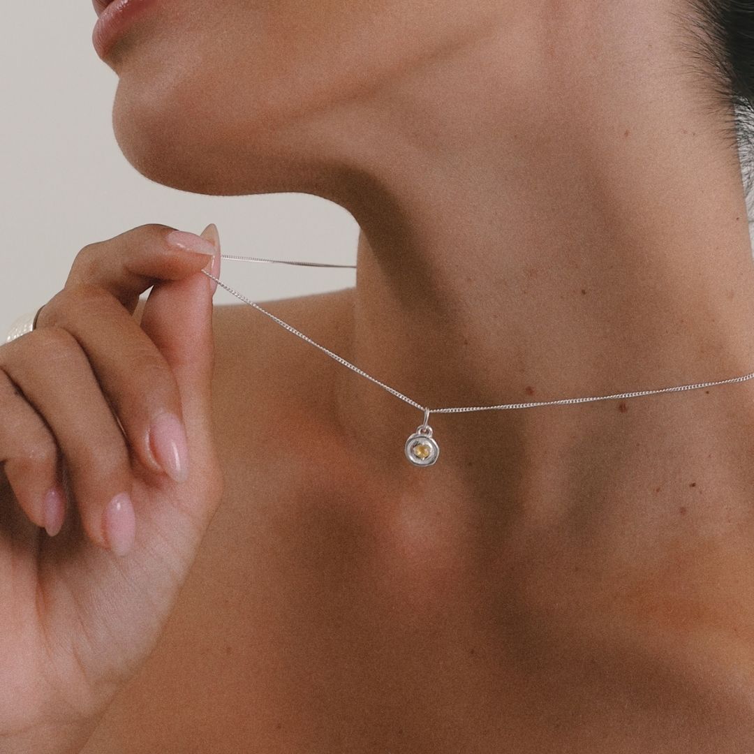 Person adjusting a delicate necklace with a small pendant.