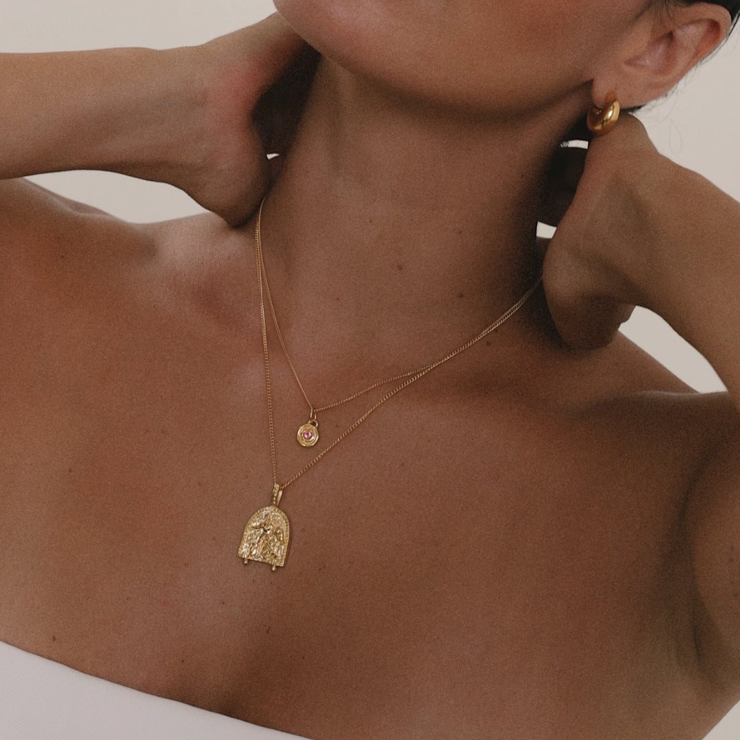 Close-up of a person wearing gold necklaces and earrings on a neutral background