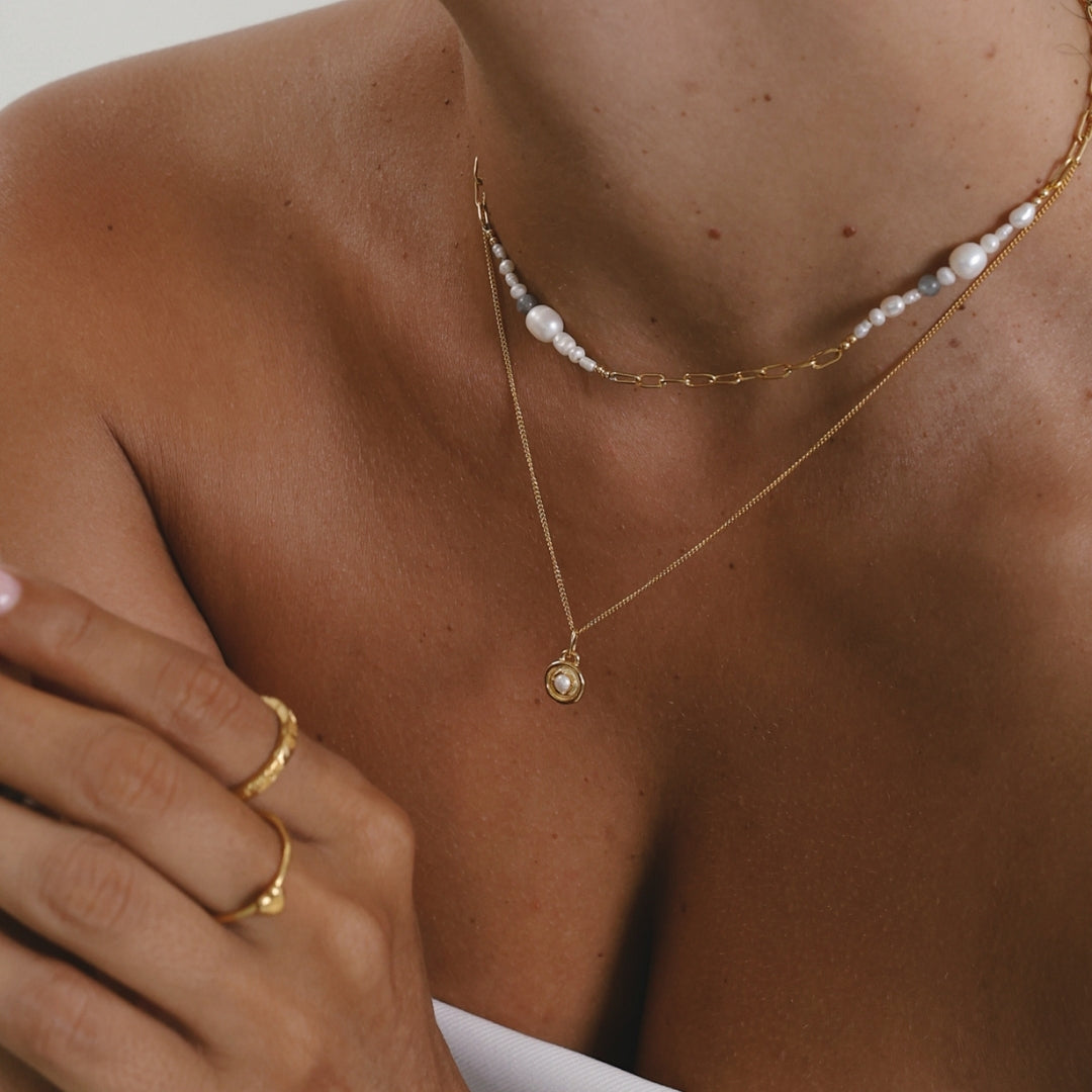 Close-up of a person wearing gold necklaces and a ring on a neutral background