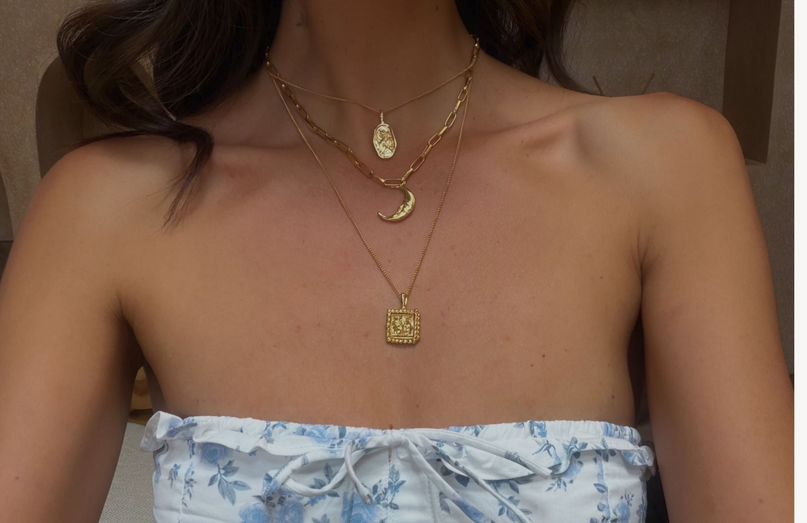 Woman wearing multiple gold necklaces with a floral strapless top.