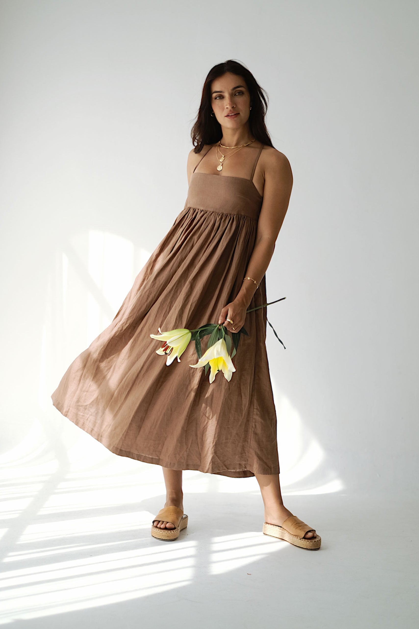 Woman in a brown dress holding flowers against a white background