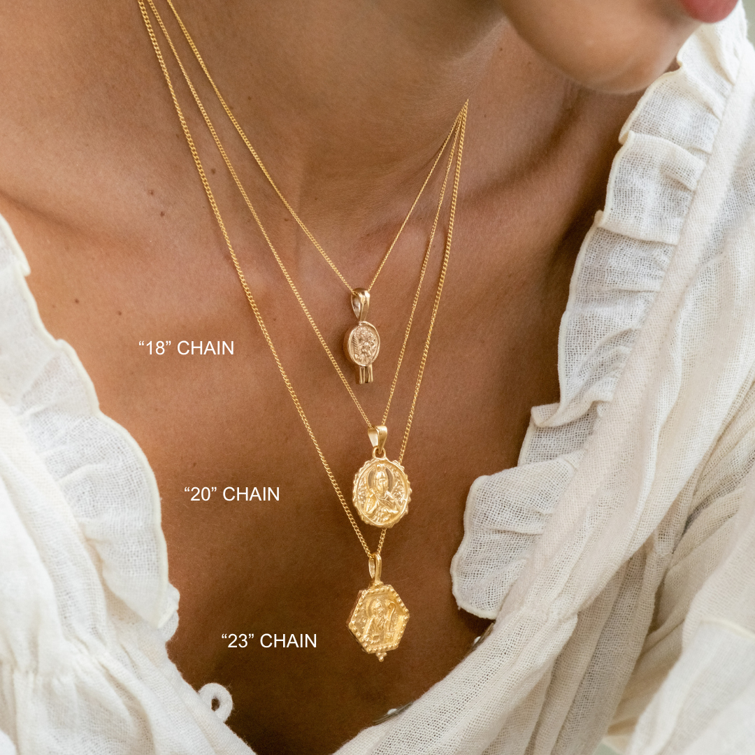 Gold necklaces with different chain lengths on a person wearing a white blouse.