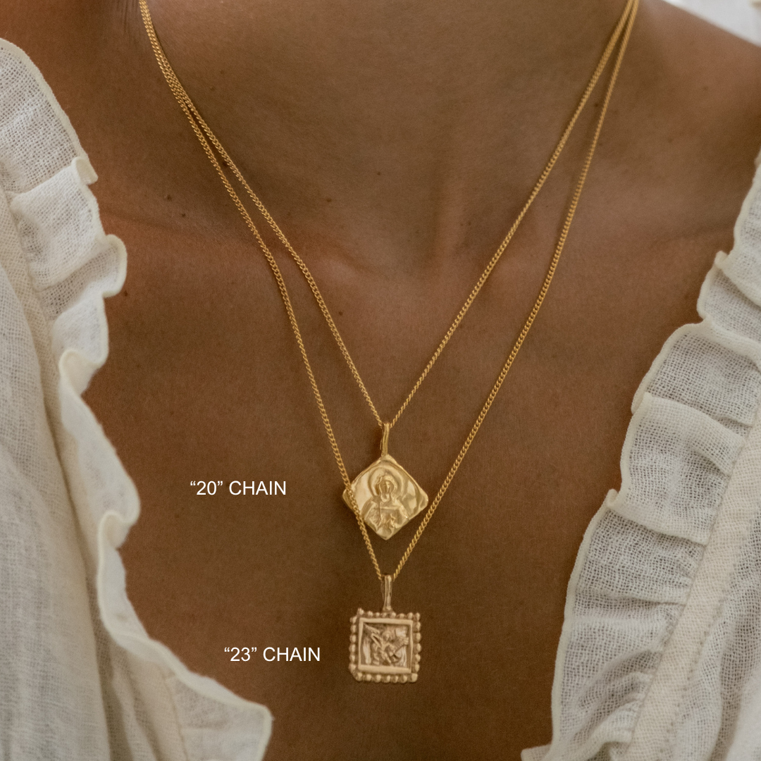 Gold necklaces with pendants on a person wearing a white blouse.
