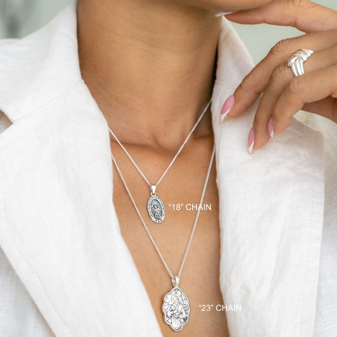Silver necklaces with pendants on a person wearing a white outfit.