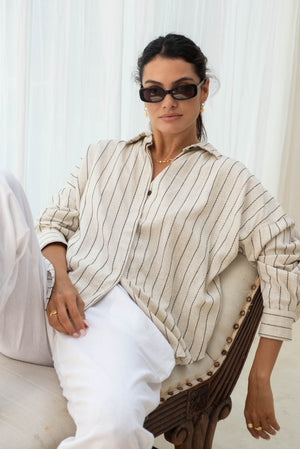 A person sitting, with sunglasses, a striped shirt, and white pants.