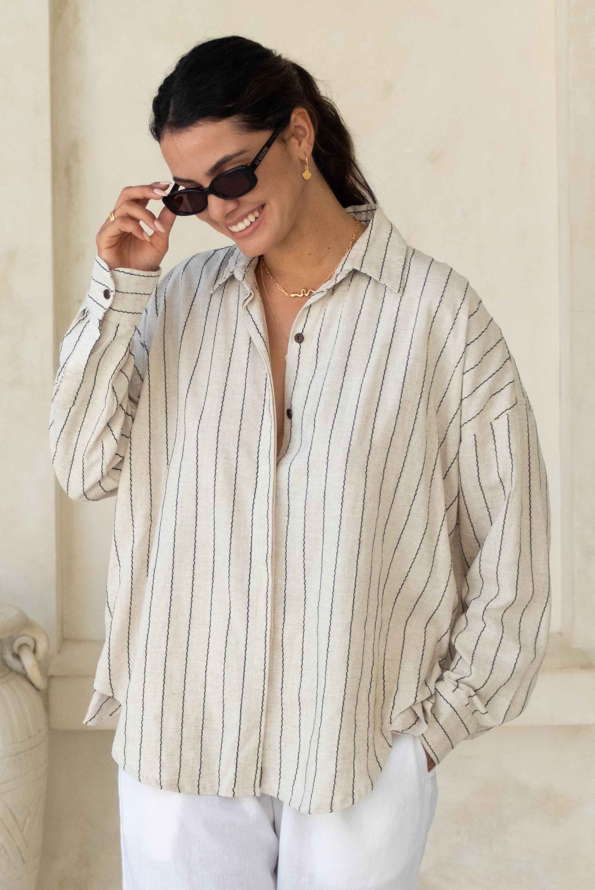 A person standing with hands in pockets, wearing a striped button-up shirt and blue pants.