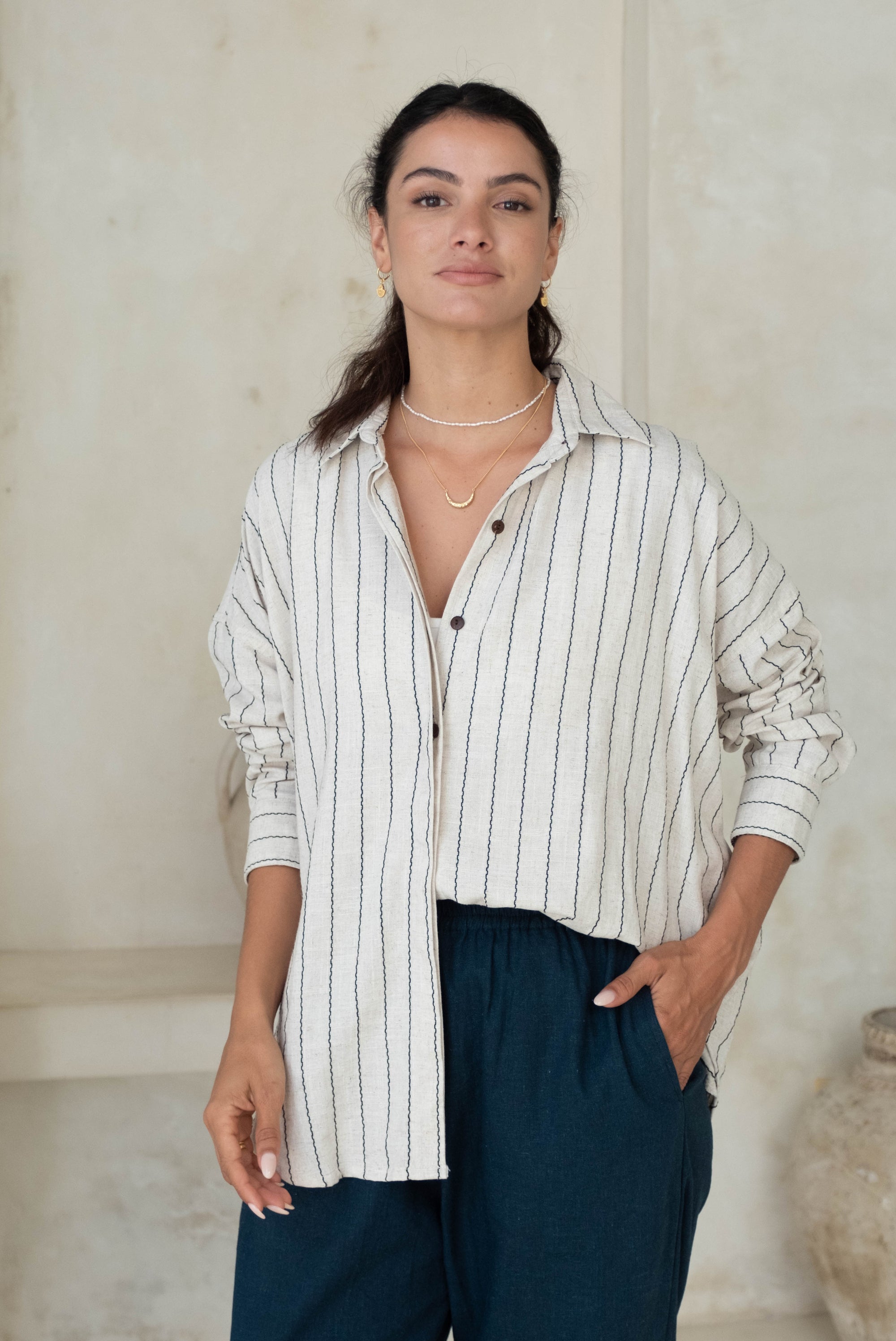 A person standing with hands in pockets, wearing a striped button-up shirt and blue pants.