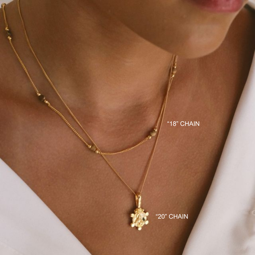 Gold necklace with two chain lengths displayed on a person's neck.