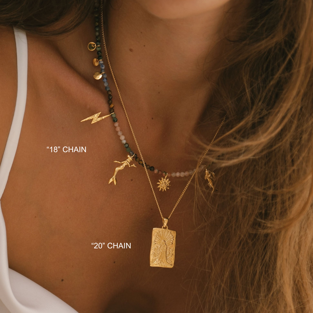 Close-up of a person wearing gold necklaces with various pendants on a neutral background.