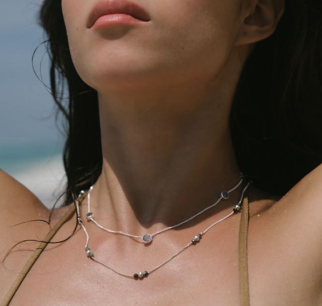 Woman at the beach wearing layered necklaces with a relaxed summer look