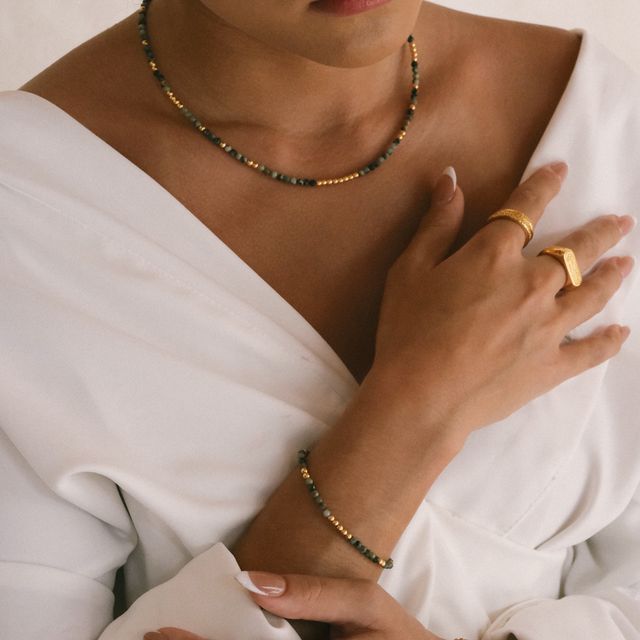Fashion portrait of a woman wearing gold earrings, gemstone necklace, bracelet, and multiple gold rings