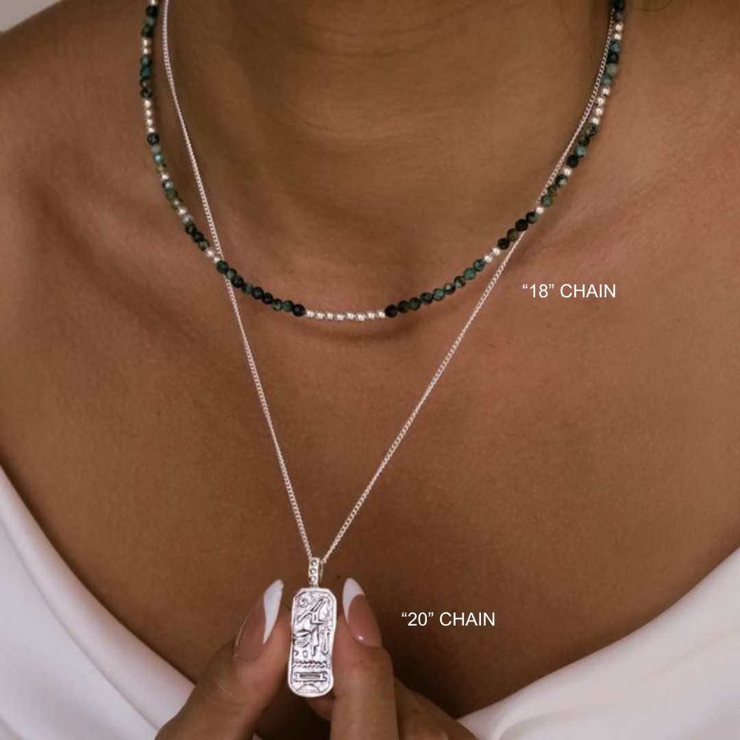 Two necklaces with different chain lengths on a person's neck, one held by a hand.